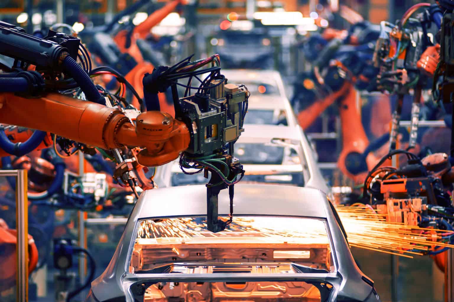 a high-tech automotive manufacturing facility where multiple robotic arms, painted in bright orange, are assembling car bodies