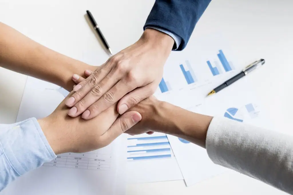 Team of coworkers stacking their hands on top of each other over reports