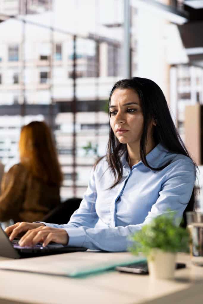 Woman plant manager sitting at her desk in an open office, working on laptop