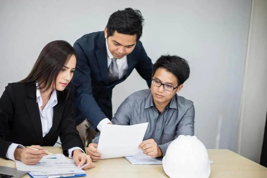Three supplier engineers, two men and one woman, are sitting at table, looking over documents